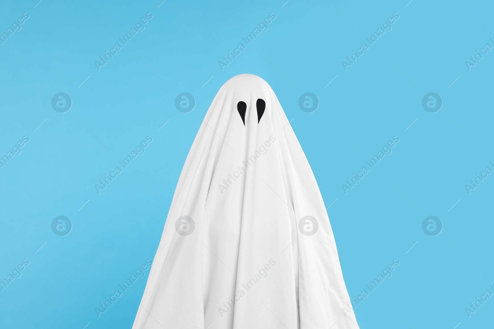 Photo of Woman in white ghost costume on light blue background. Halloween celebration