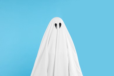 Photo of Woman in white ghost costume on light blue background. Halloween celebration