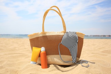 Photo of Sunscreens, bag and swimsuit top on sandy beach. Sun protection