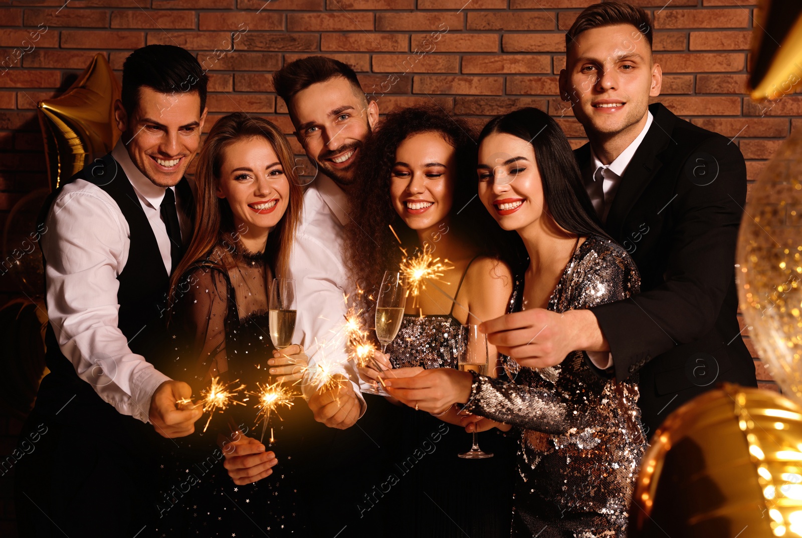 Photo of Happy friends with glasses of sparkling wine and sparklers celebrating New Year indoors