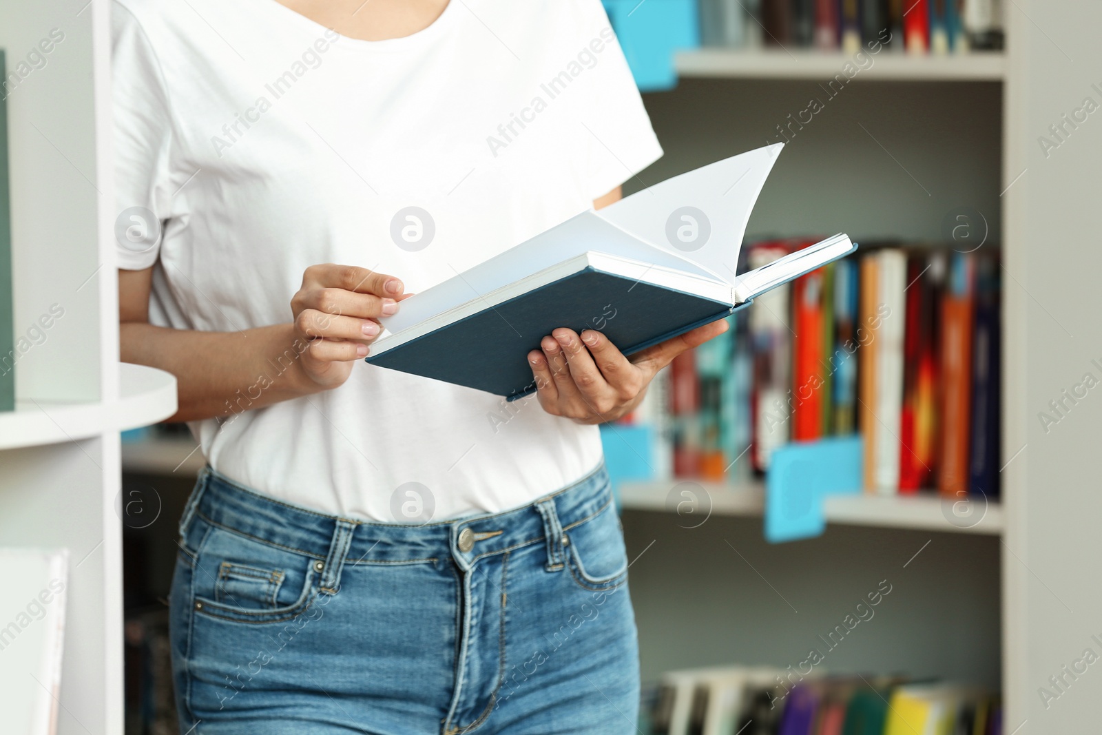 Photo of Young woman with book near shelving unit in library, closeup