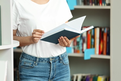 Young woman with book near shelving unit in library, closeup