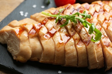 Photo of Tasty cut grilled chicken fillet with arugula on slate plate, closeup