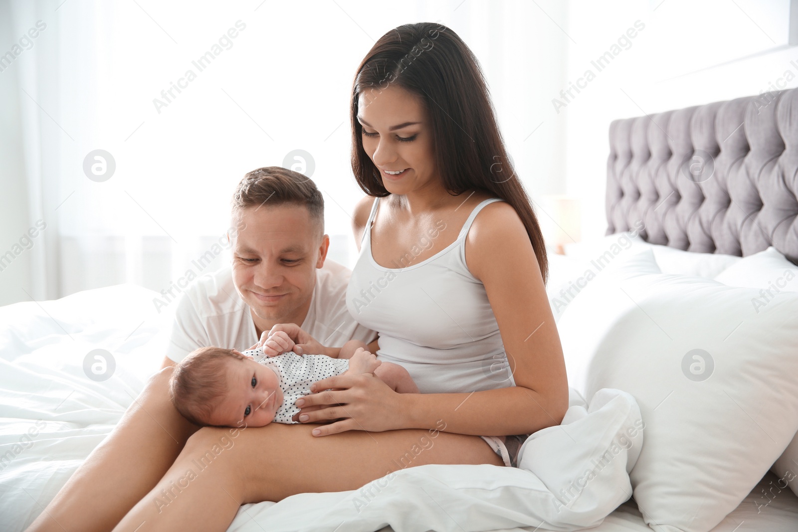 Photo of Happy couple with their newborn baby on bed