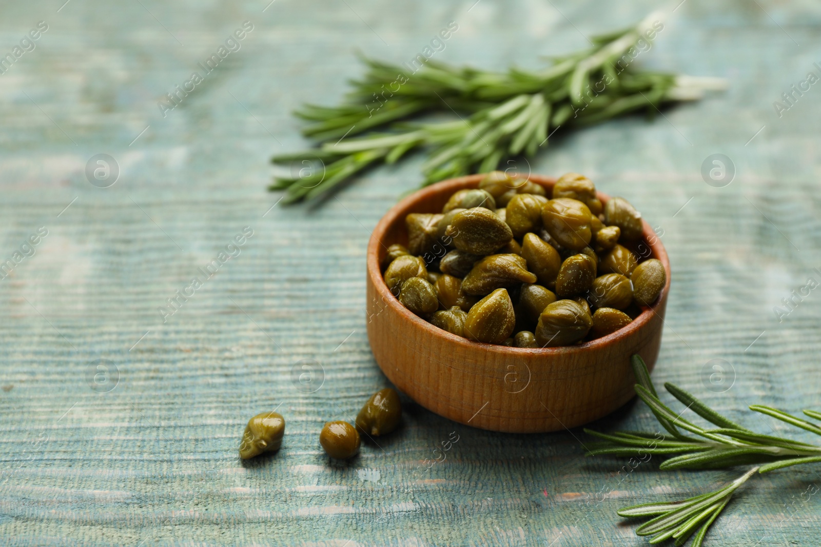 Photo of Tasty capers and rosemary on turquoise wooden table, space for text