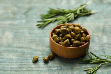 Photo of Tasty capers and rosemary on turquoise wooden table, space for text