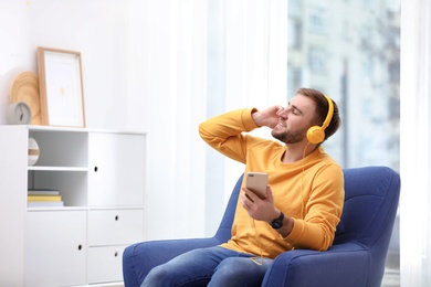 Photo of Young man with headphones and mobile device sitting in armchair at home