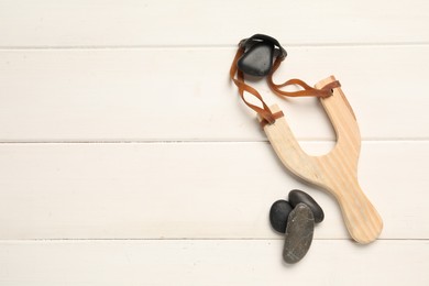 Photo of Slingshot with stones on white wooden background, flat lay. Space for text