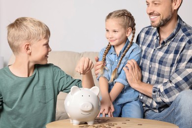 Happy family putting coin into piggy bank at home