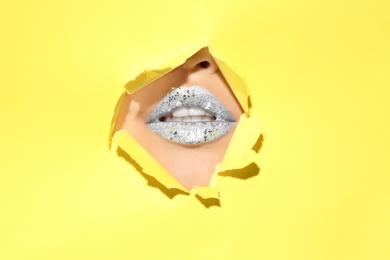 View of beautiful young woman with creative lips makeup through hole in color paper