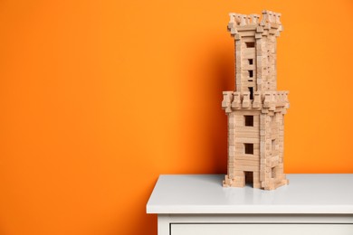 Wooden tower on white chest of drawers near orange wall, space for text. Children's toy