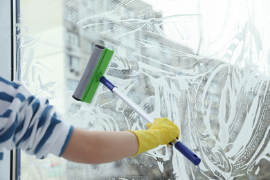 Photo of Woman cleaning window with squeegee at home, closeup. Space for text