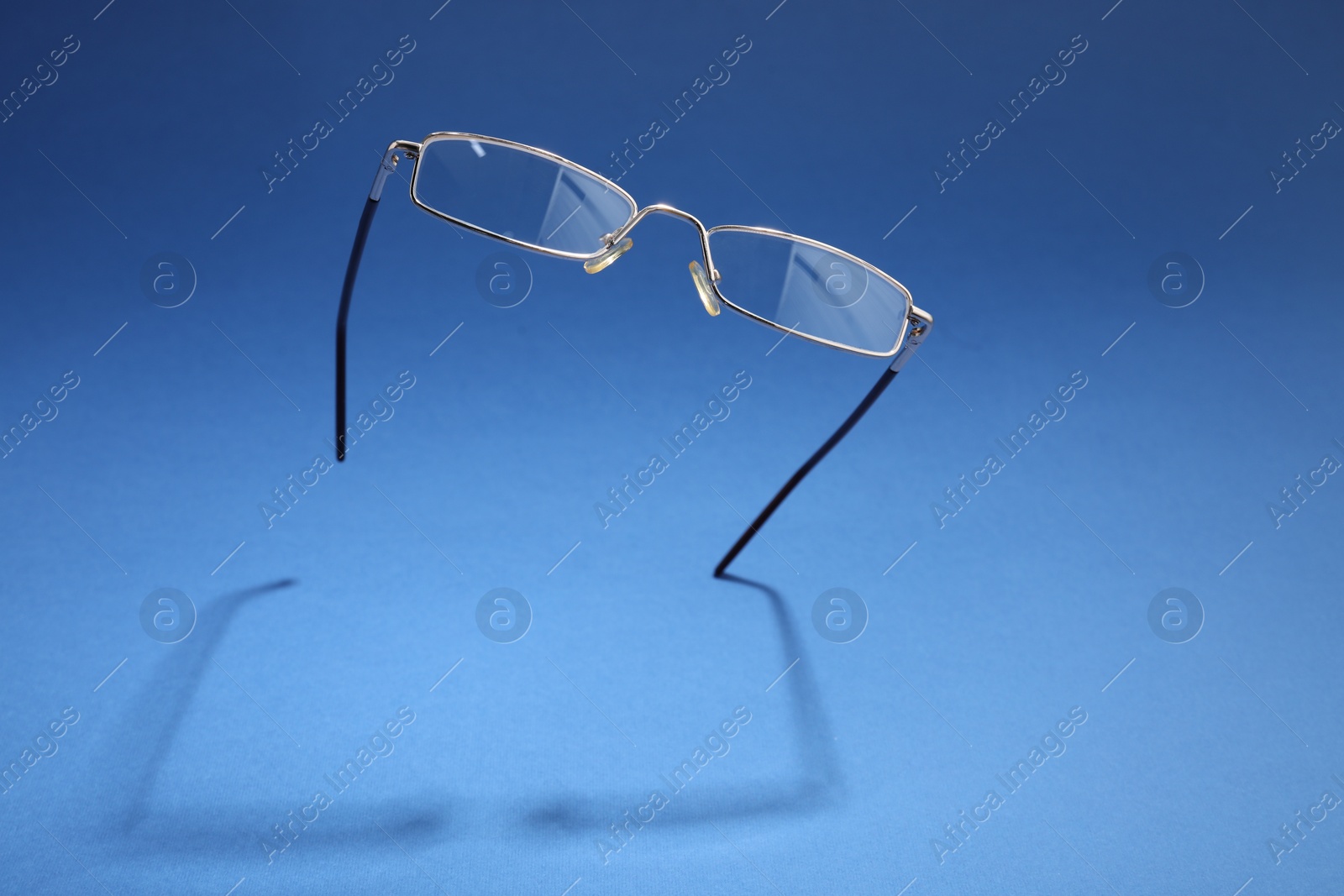 Photo of Stylish pair of glasses with metal frame on blue background, space for text