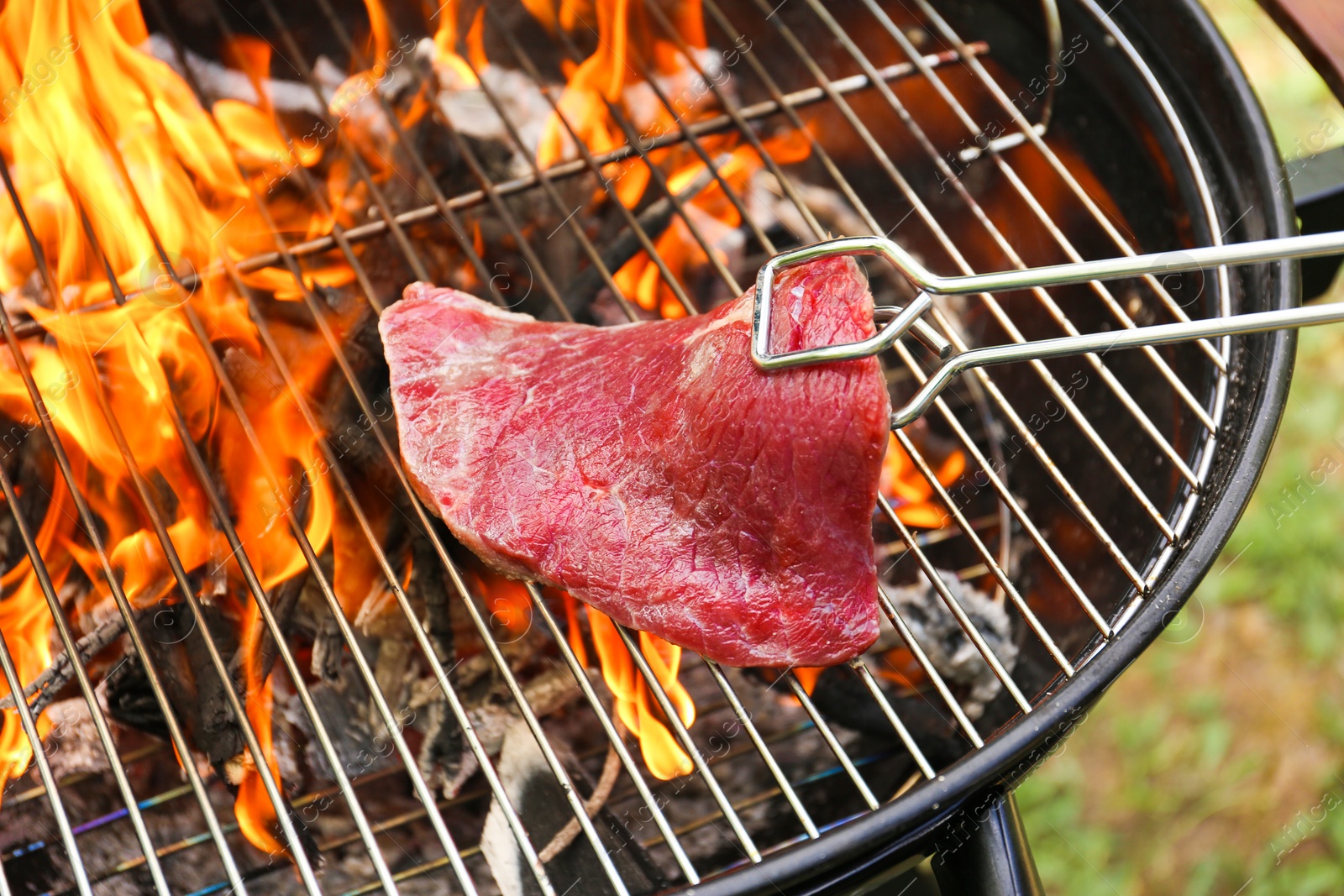 Photo of Tasty meat on barbecue grill with fire flames outdoors, closeup