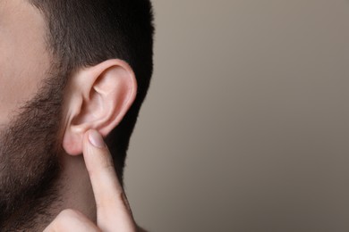 Photo of Man pointing at his ear on grey background, closeup. Space for text