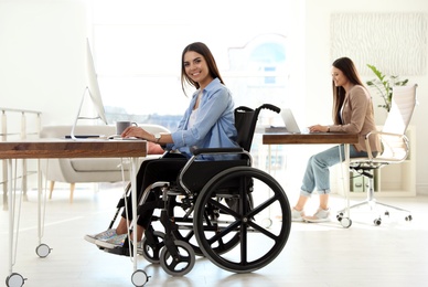 Photo of Young woman in wheelchair using computer at workplace