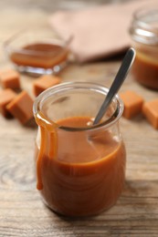 Tasty salted caramel and spoon in glass jar on wooden table