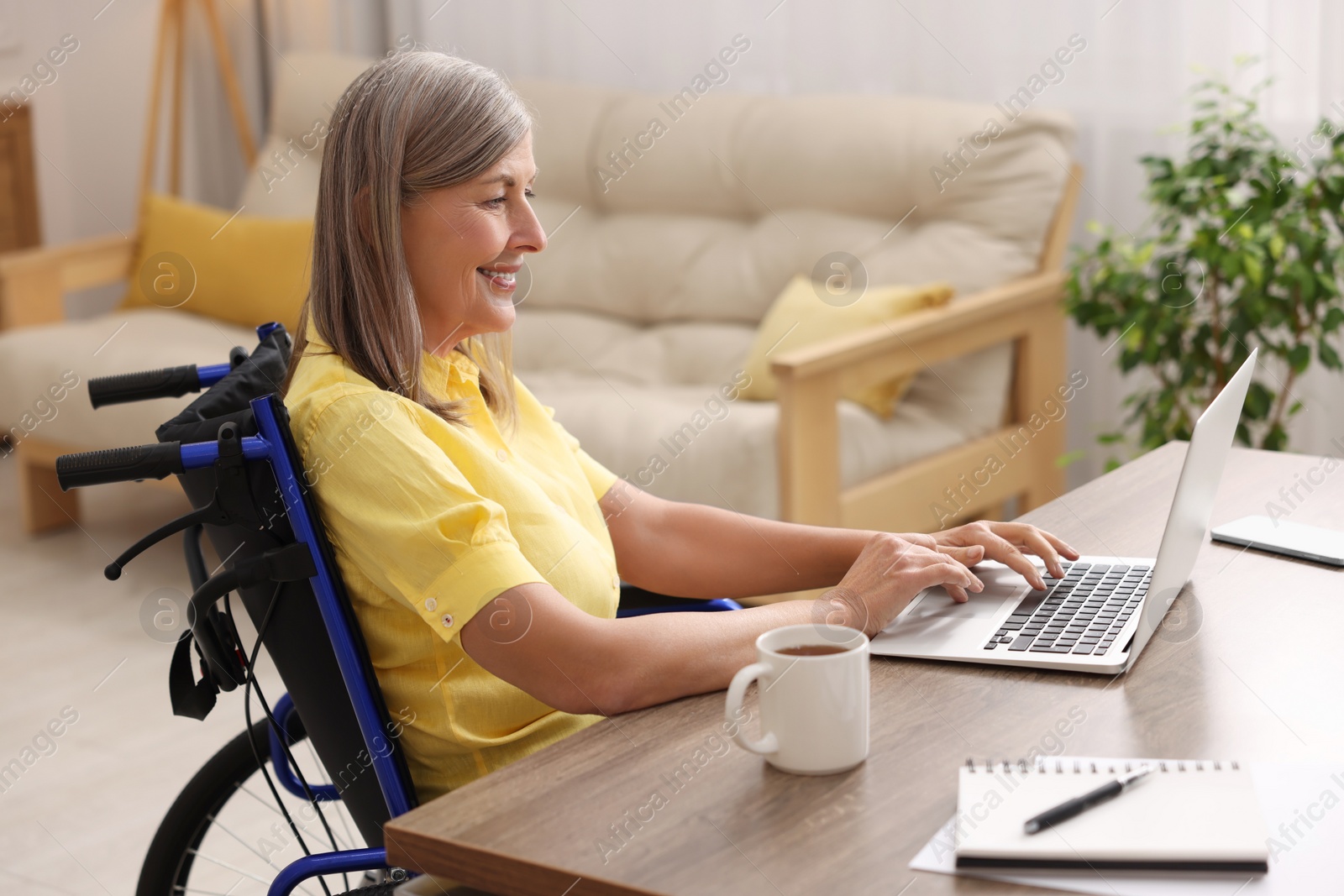 Photo of Woman in wheelchair using laptop at table in home office