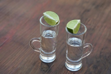 Photo of Mexican tequila shots with lime slices on wooden table