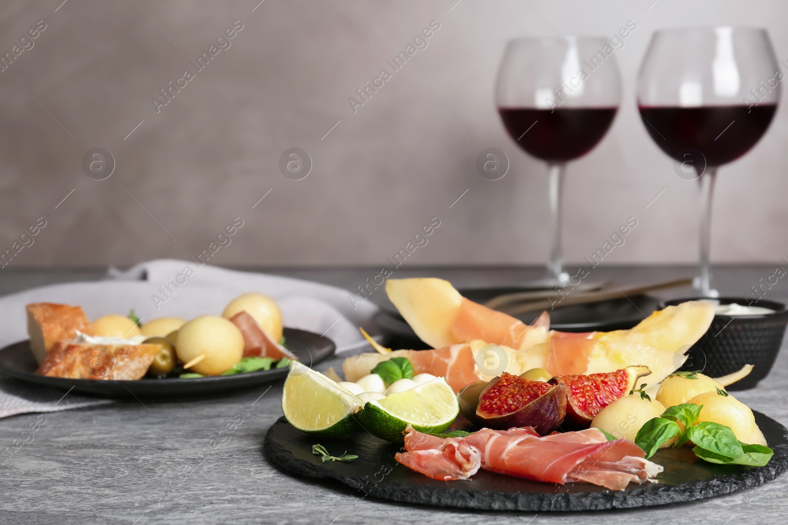 Photo of Slate plate with melon slices and prosciutto on table