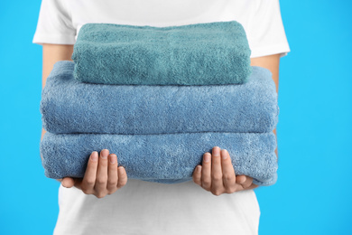 Woman holding fresh towels on light blue background, closeup