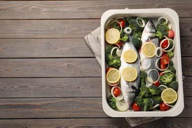 Photo of Raw fish with vegetables and lemon in baking dish on wooden table, top view. Space for text