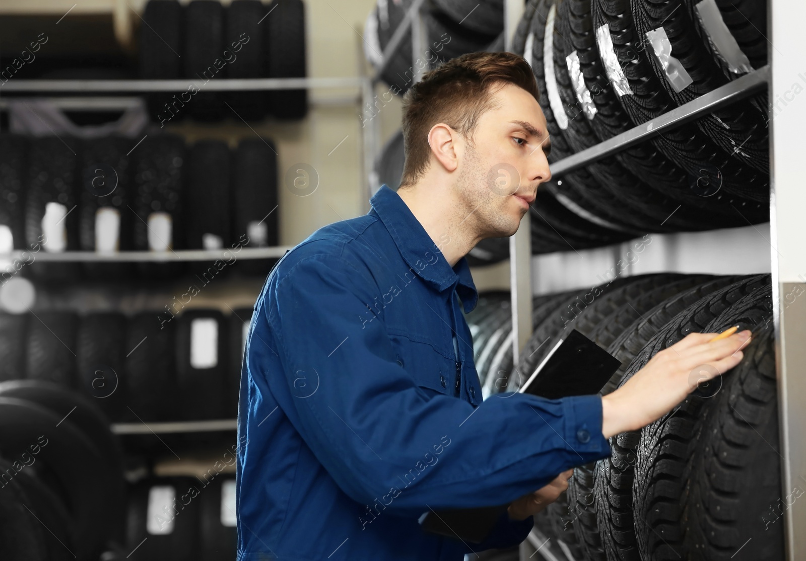 Photo of Young male mechanic with clipboard near tires in automobile service center