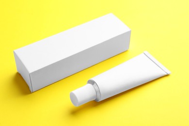 Photo of Blank white tube of ointment with cardboard box on yellow background. Space for text