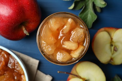 Photo of Tasty apple jam in glass jar and fresh fruits on blue table, flat lay