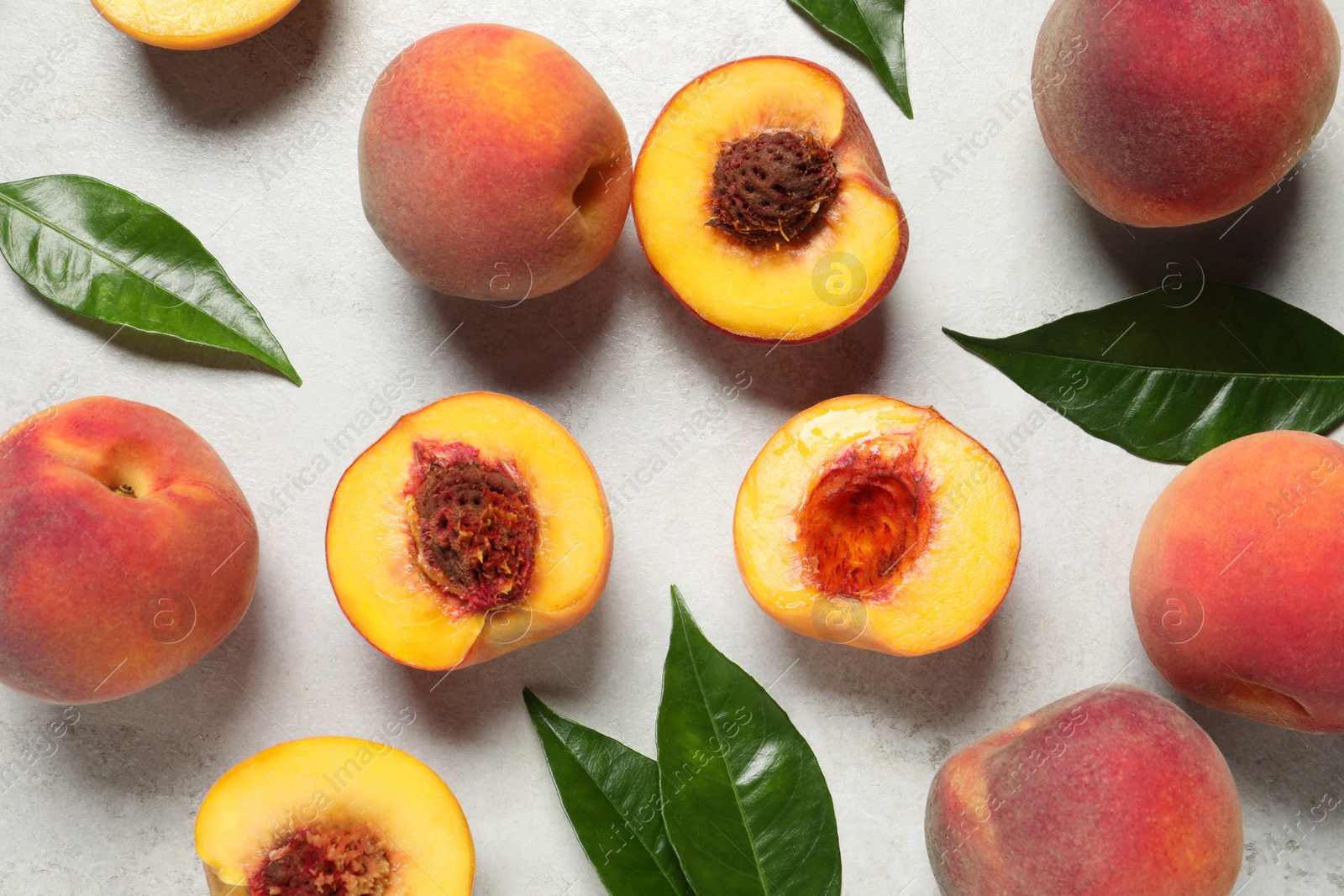 Photo of Delicious ripe peaches and leaves on light grey textured table, flat lay