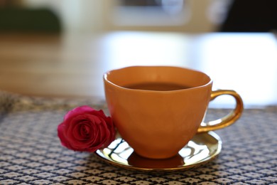 Photo of Cup of hot drink and red rose on table indoors, closeup