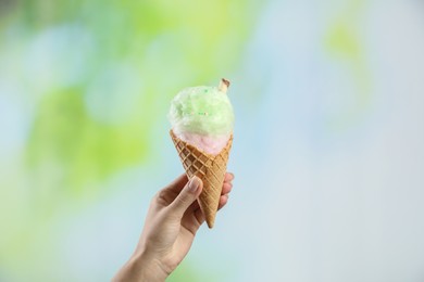 Woman holding waffle cone with cotton candy on blurred background, closeup