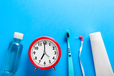 Photo of Toothbrushes, teeth care products and alarm clock on light blue background, flat lay. Space for text