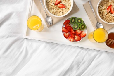 Photo of Tasty breakfast served in bed. Oatmeal, juice, fruits and honey on tray, top view. Space for text