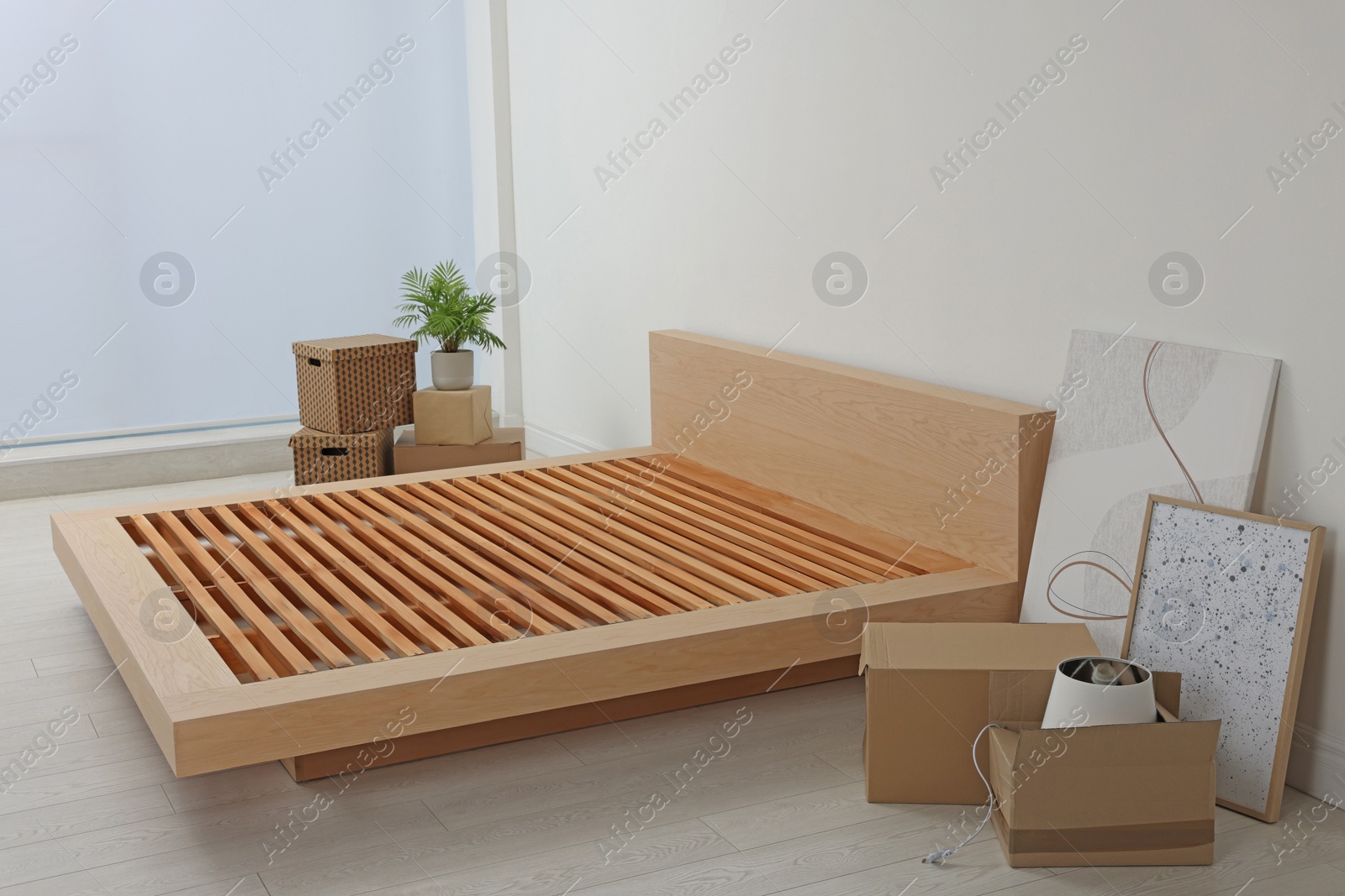 Photo of New wooden bed frame, moving boxes and decor elements indoors