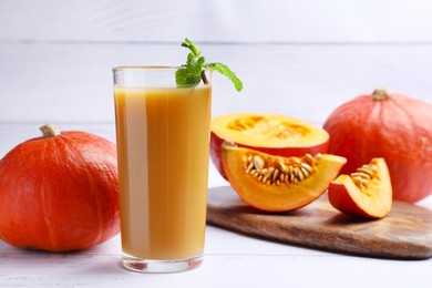 Photo of Tasty pumpkin juice in glass and pumpkins on white wooden table