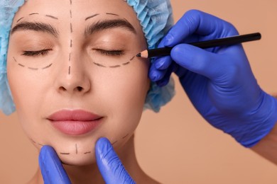Photo of Doctor drawing marks on woman's face for cosmetic surgery operation against beige background, closeup