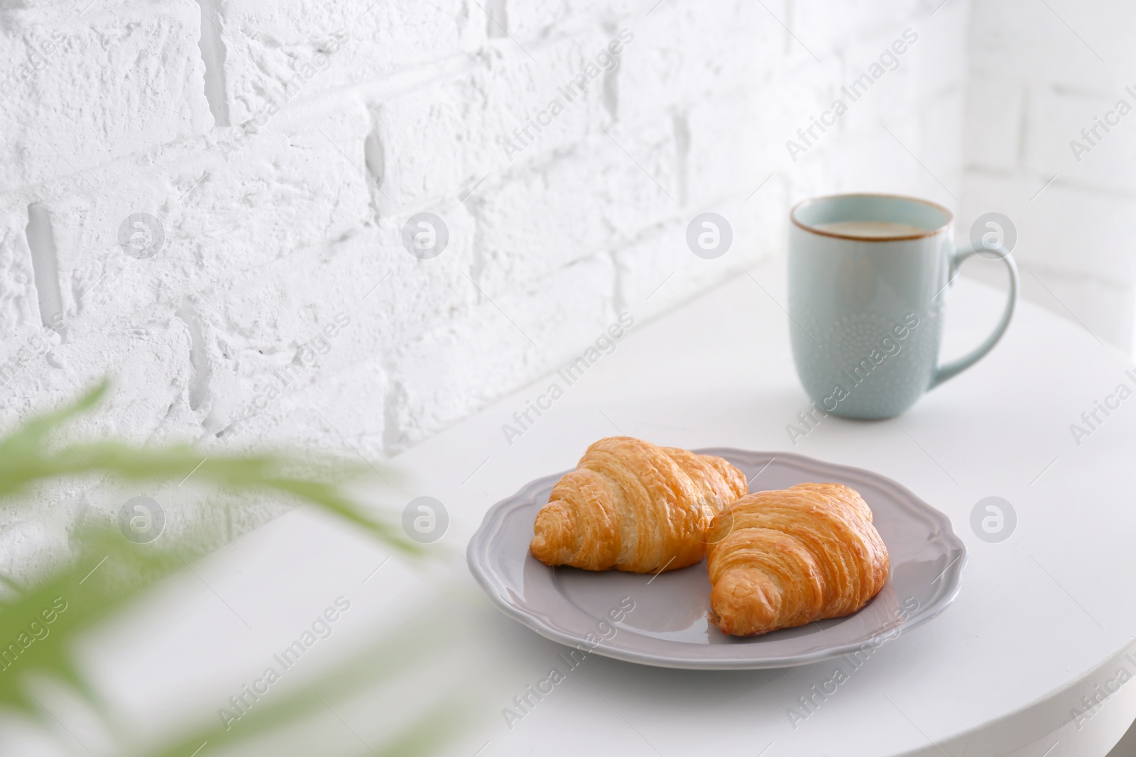 Photo of Cup and plate with tasty croissants on table