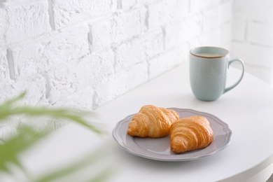 Cup and plate with tasty croissants on table