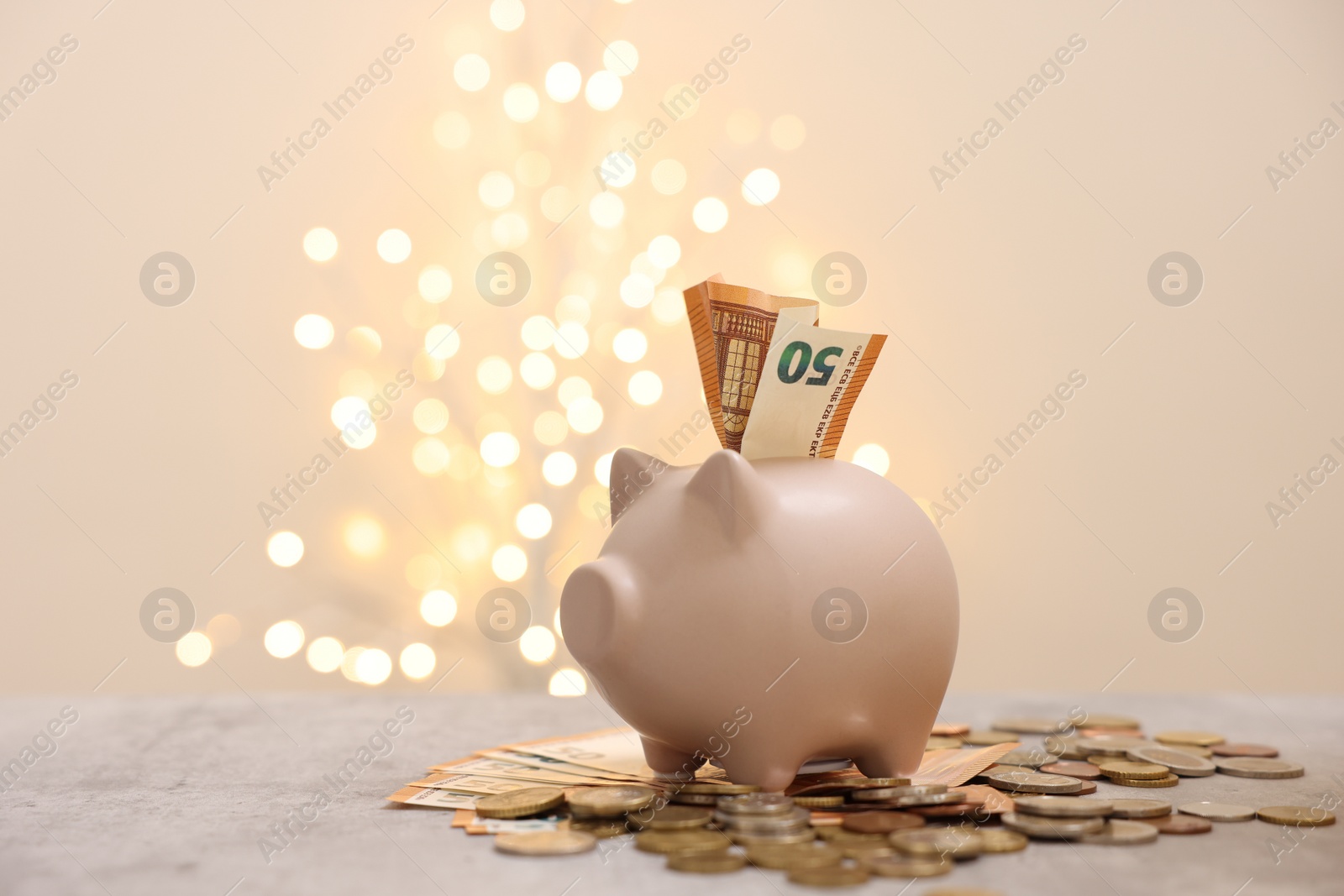 Piggy bank with euro banknote and coins on grey table against blurred lights Photo of Piggy bank with euro banknote and coins on grey table against blurred lights