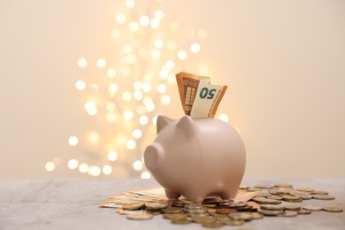 Photo of Piggy bank with euro banknote and coins on grey table against blurred lights