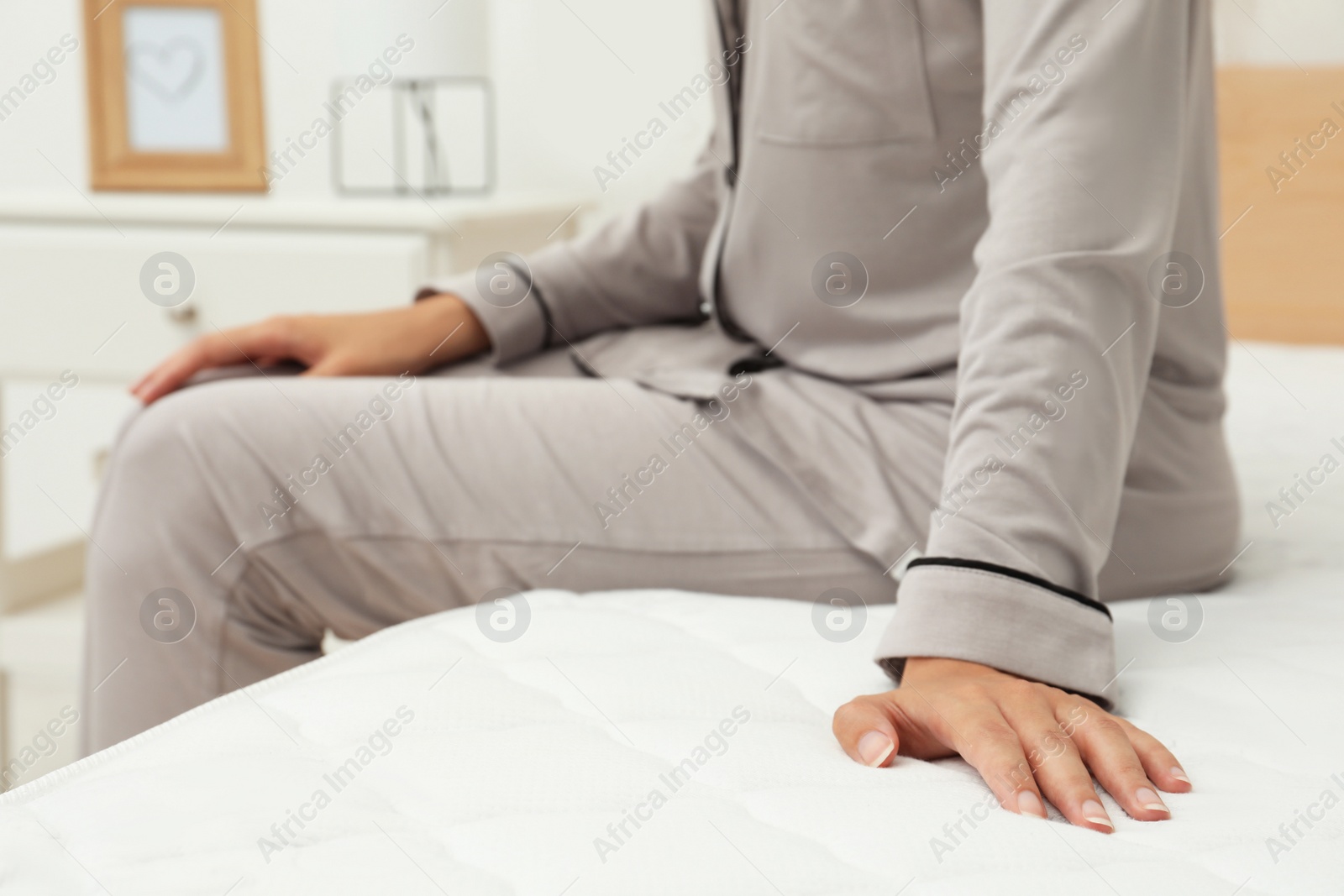 Photo of African American woman sitting on soft mattress in bedroom, closeup