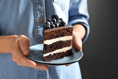 Photo of Woman holding plate with slice of chocolate sponge berry cake on grey background, closeup