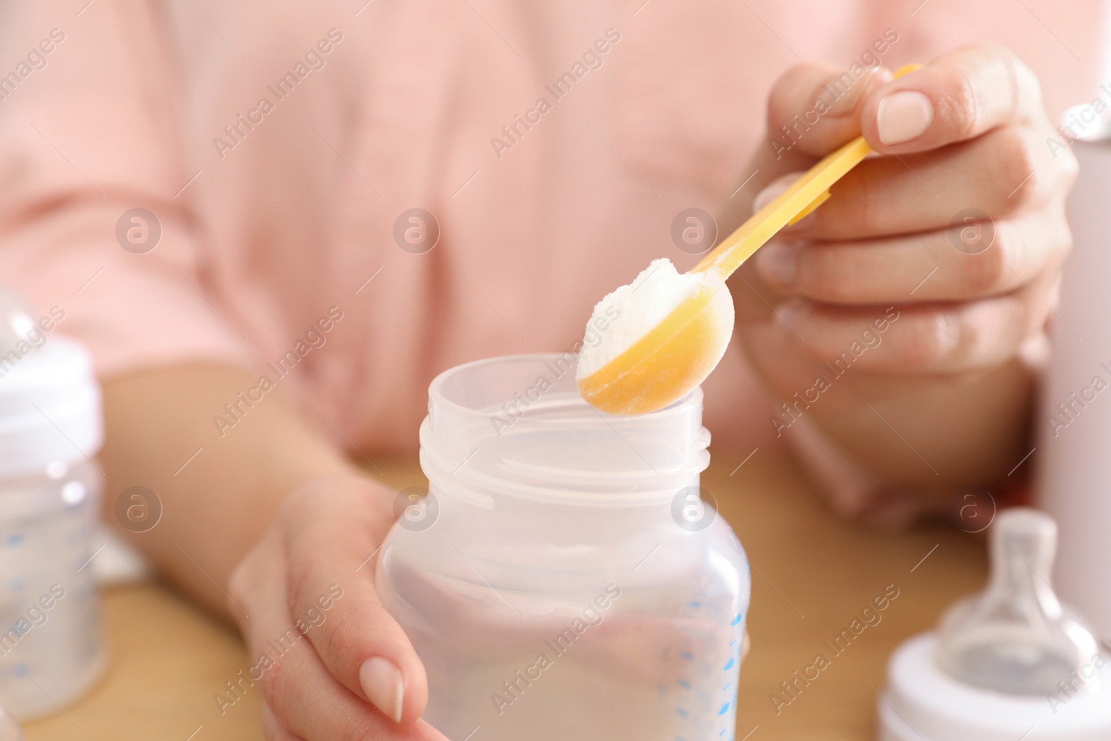 Photo of Woman preparing infant formula at table, closeup. Baby milk