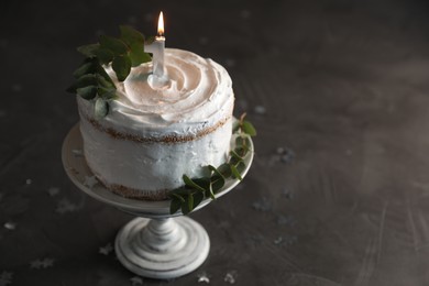 Photo of Tasty Birthday cake with burning candle and eucalyptus branches on grey table
