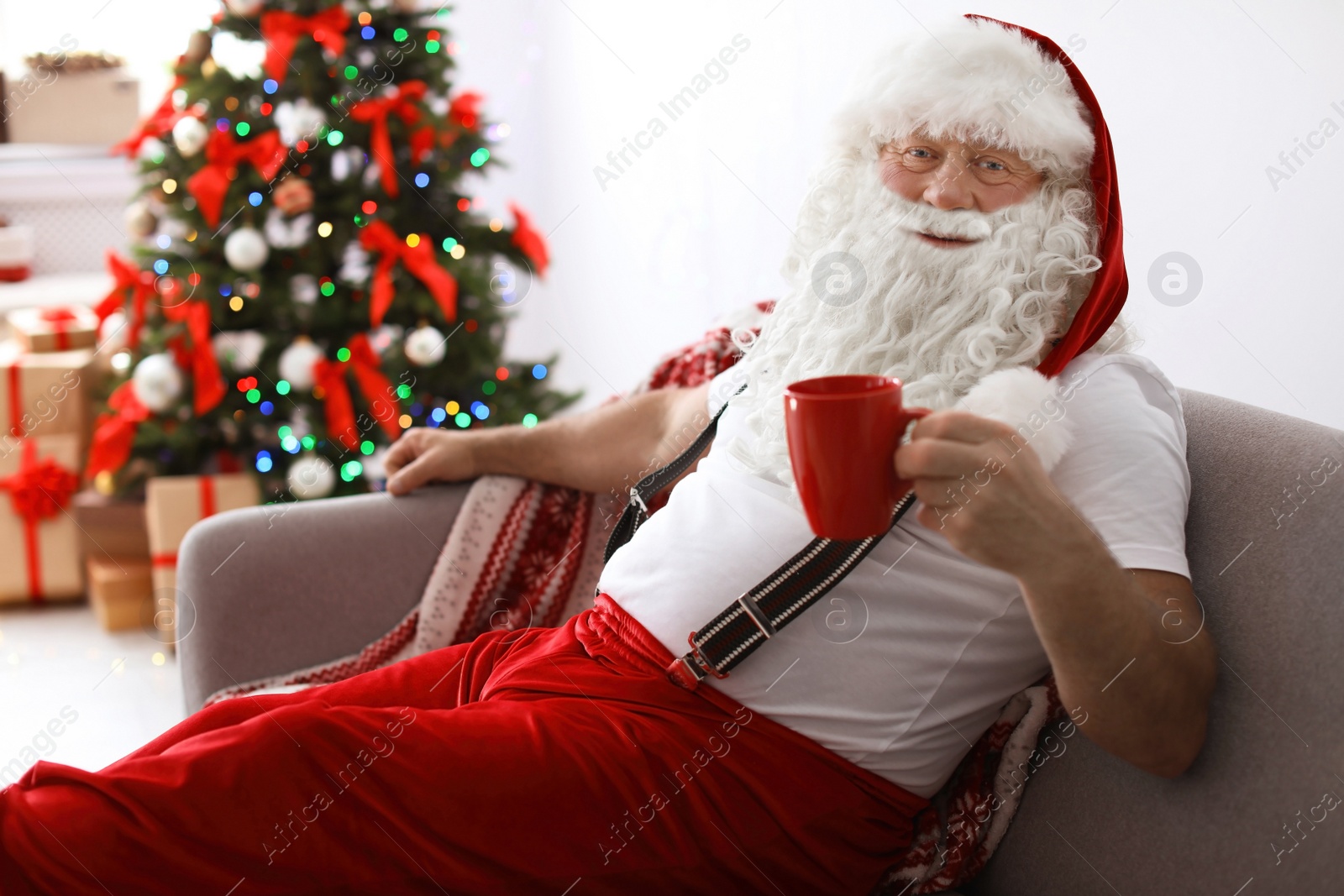Photo of Authentic Santa Claus resting with cup of tea on sofa indoors