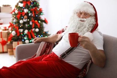 Authentic Santa Claus resting with cup of tea on sofa indoors