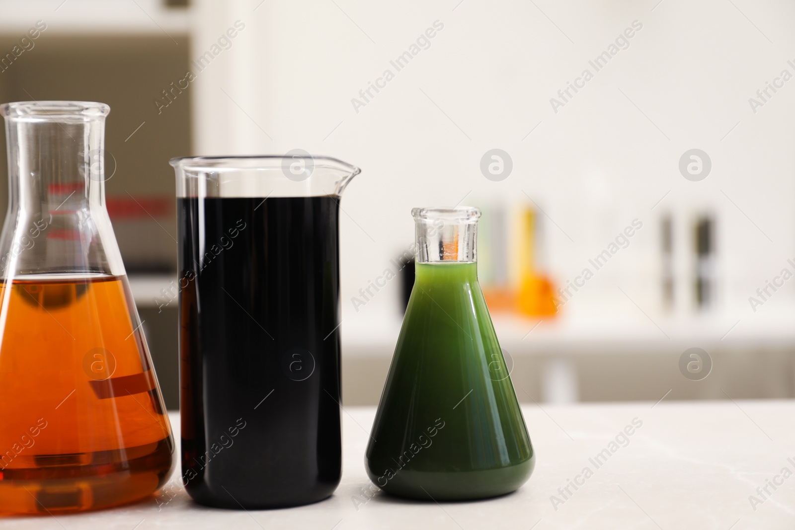 Photo of Flasks and beaker with different types of crude oil on light marble table, space for text