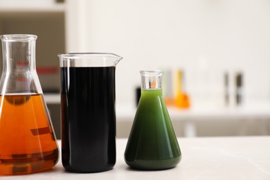 Flasks and beaker with different types of crude oil on light marble table, space for text