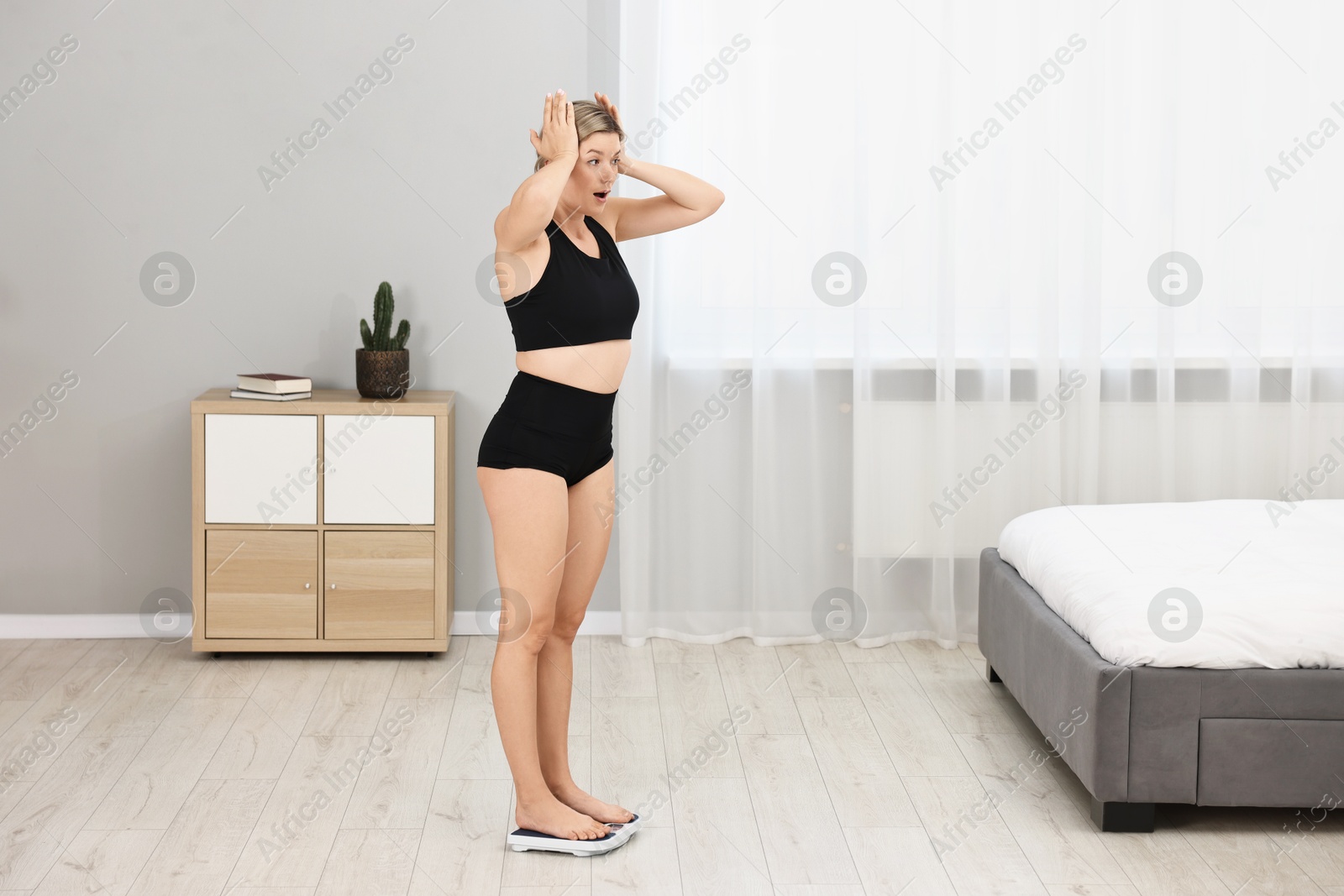 Photo of Surprised woman standing on floor scales at home
